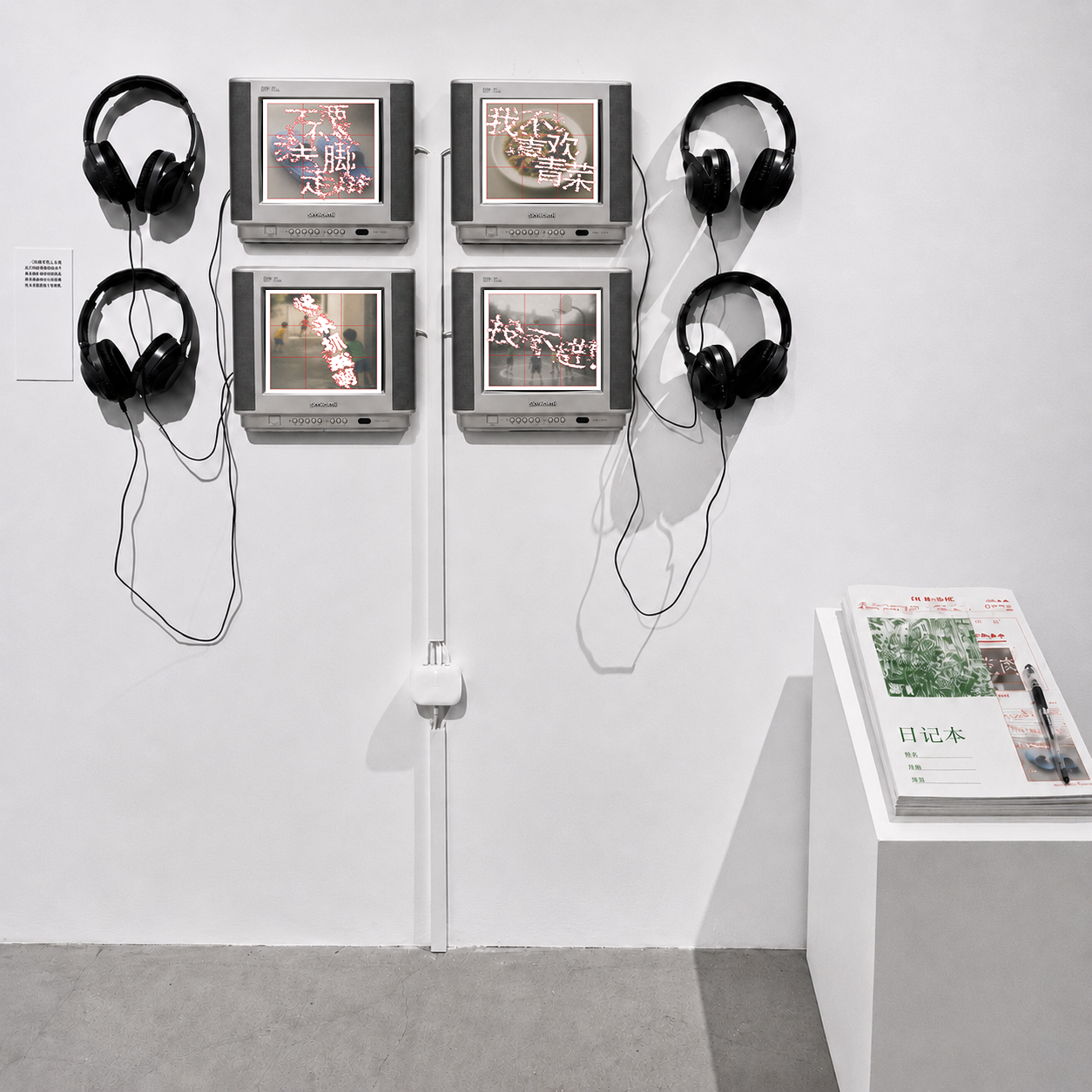 Exhibition — four-screen wall with headphones and booklet plinth